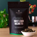 August Superbloom Sweet Lemon Oolong Tea package with a bowl of tea leaves on a wooden surface.