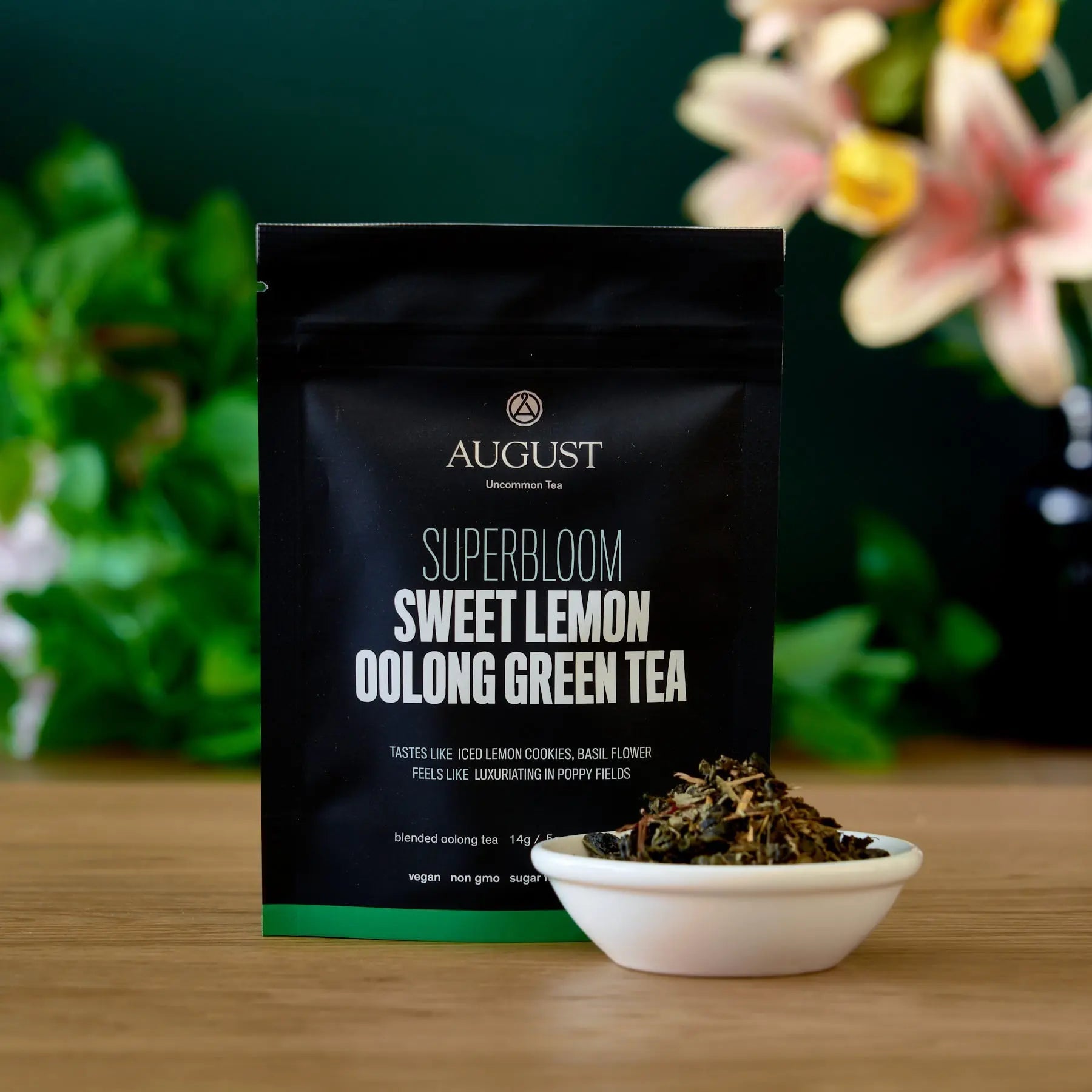 August Superbloom Sweet Lemon Oolong Green Tea packaging with tea leaves in a bowl on a wooden surface.